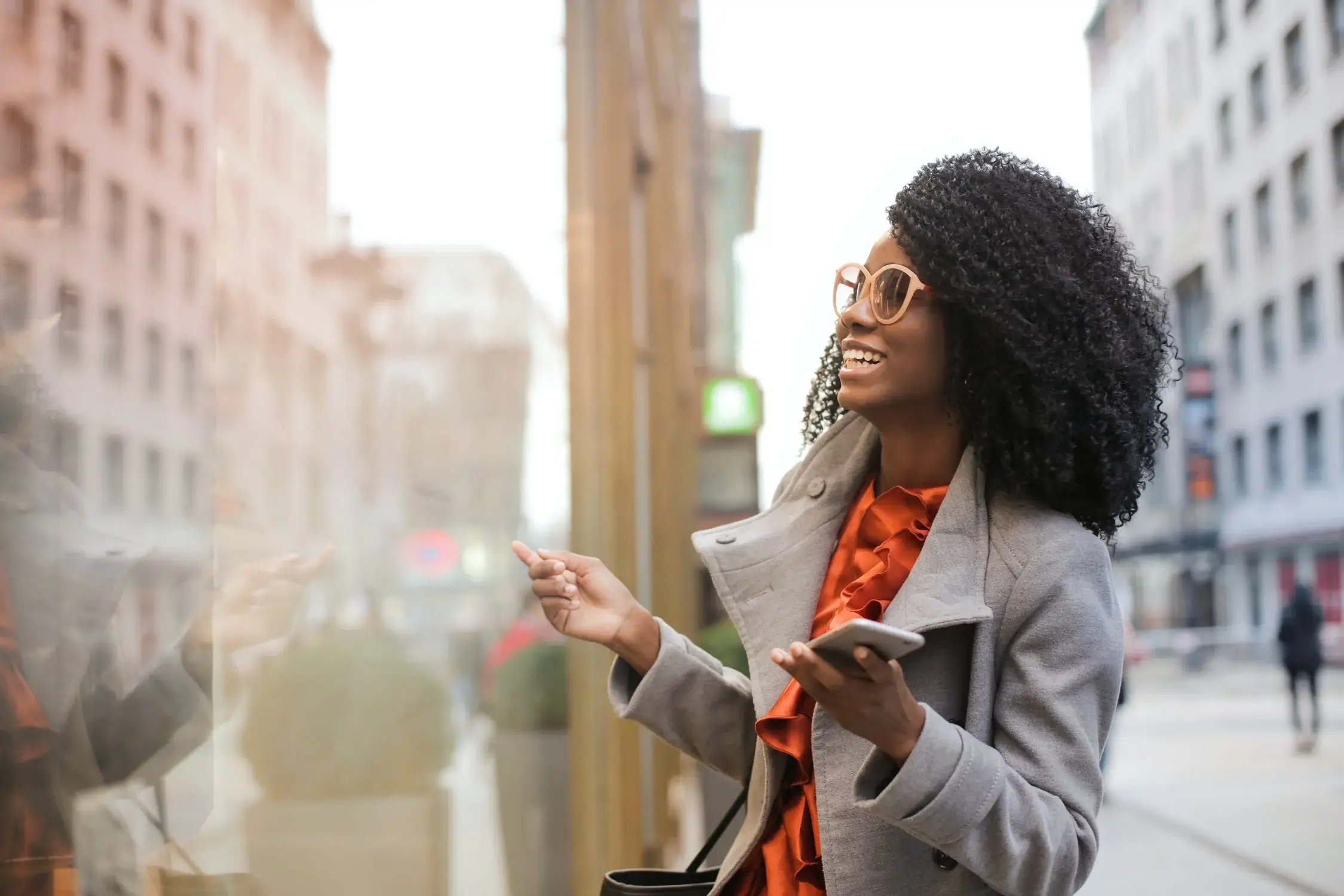 Woman smiling and looking at city street reflecting in window, Urban Tulsa lifestyle article.
