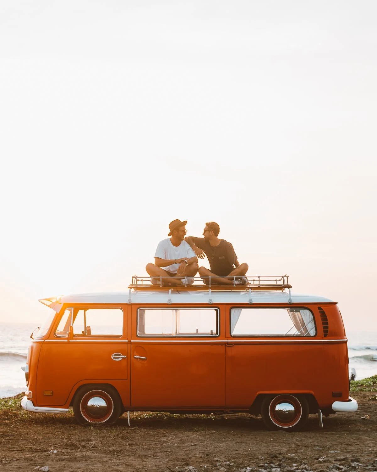 Couple relaxing on top of vintage orange camper van, RV travel planning.
