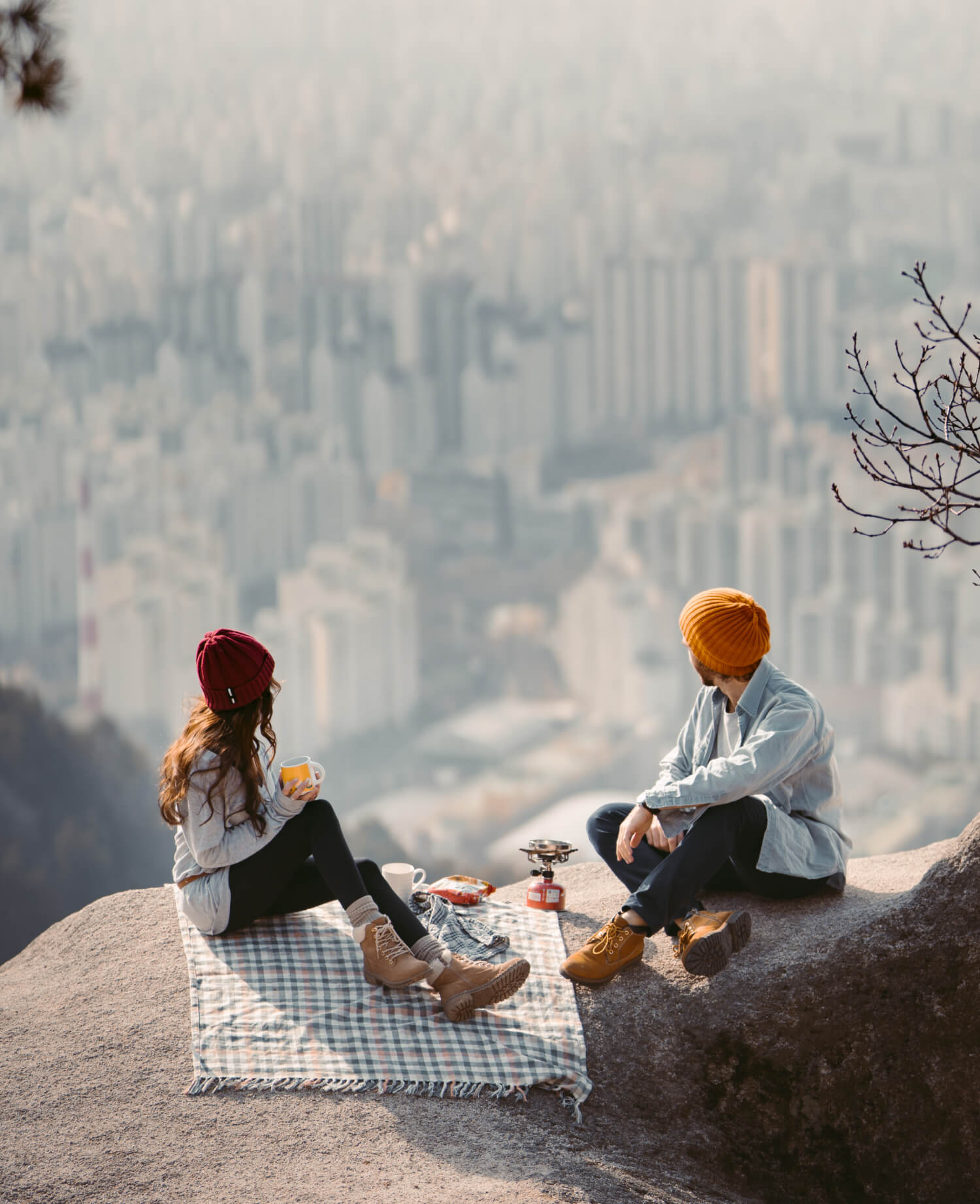 a man and woman sitting on a rock with a city in the background